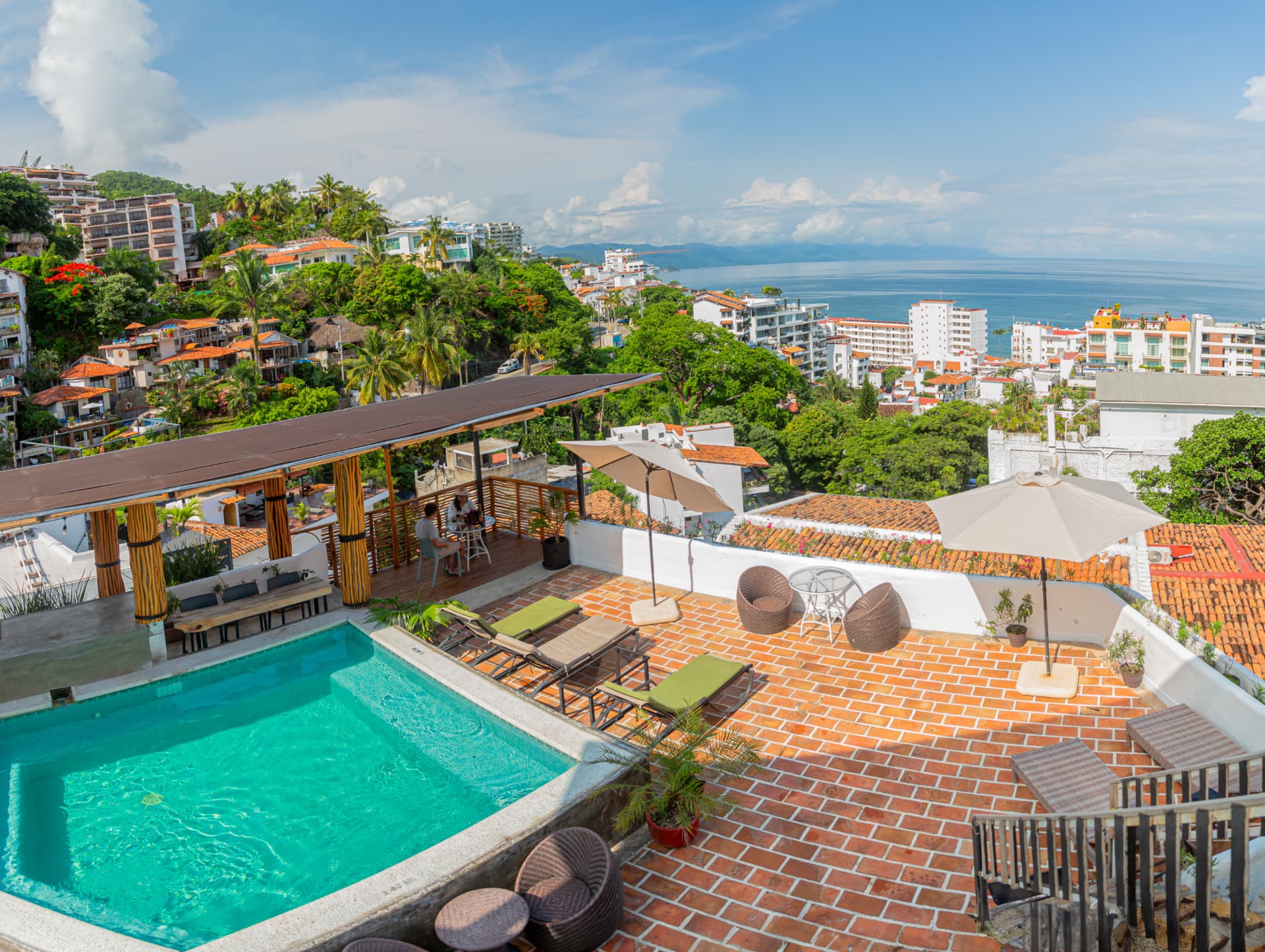 Alberca turquesa del rooftop de Amaca con camastros, terraza de ladrillo y vista a la Bahía de Banderas